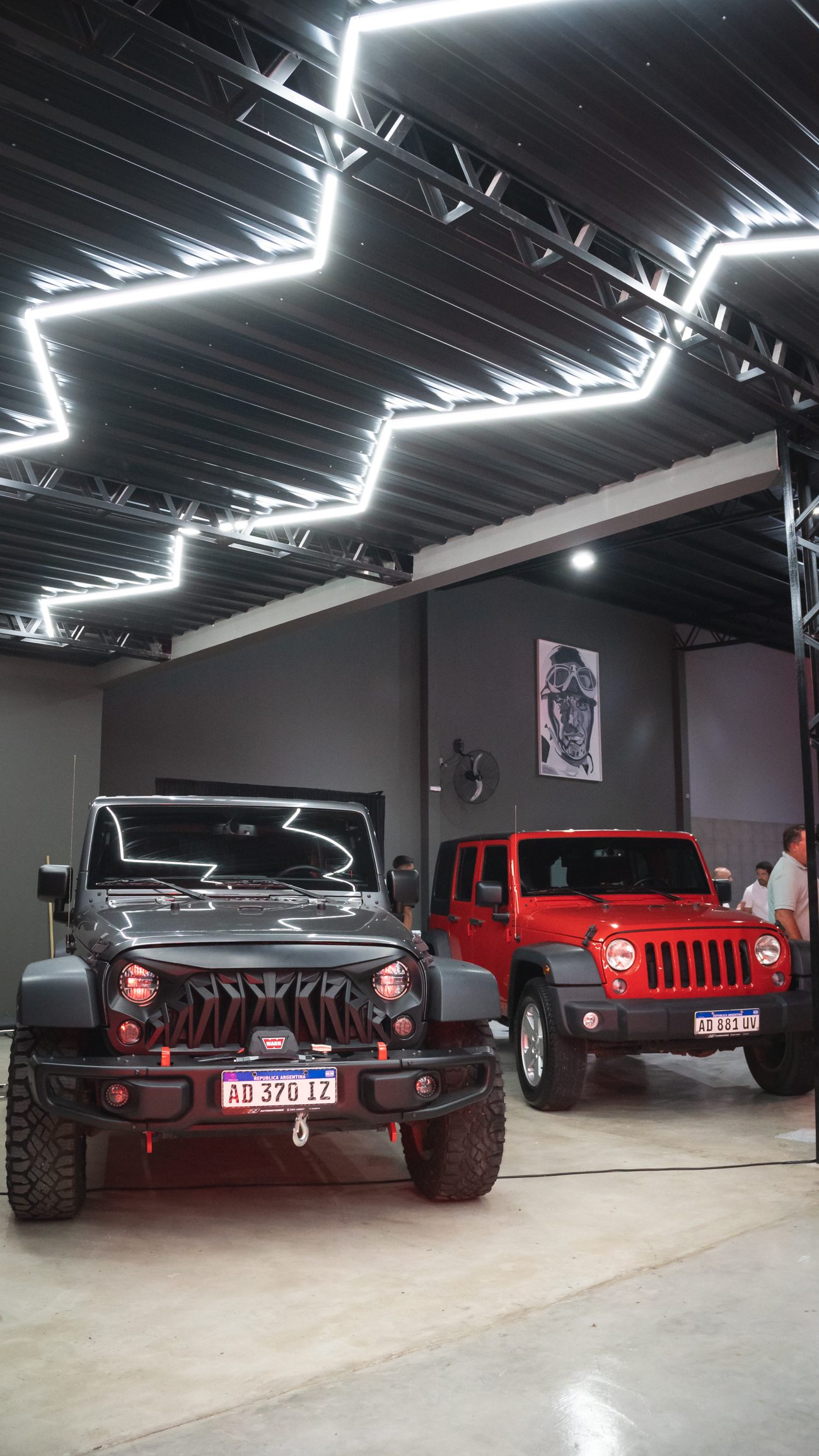 Dos Jeep Wrangler — uno negro custom y uno rojo — en el salón F27 bajo iluminación LED